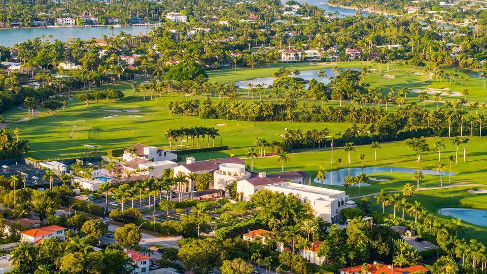 Paisagem costeira com um campo de golfe, áreas residenciais e um porto de iates.