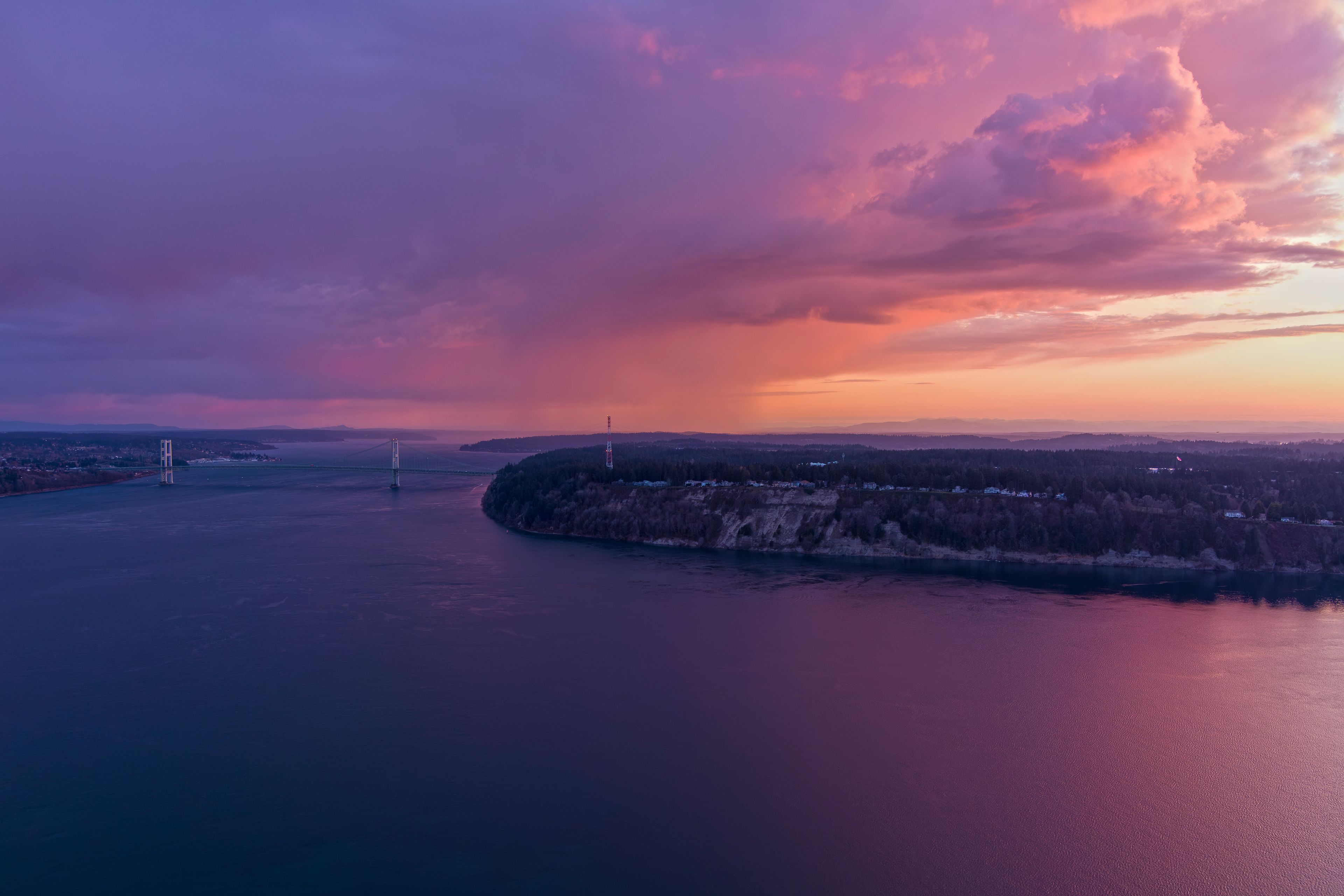 A sunset over a river with a bridge and a distant shoreline.