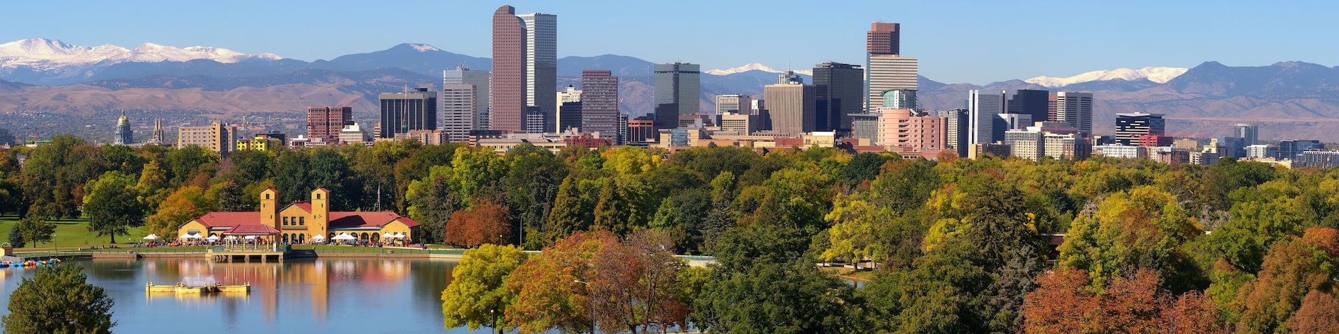 A city skyline with modern buildings, a lake with boats, and mountains in the background.