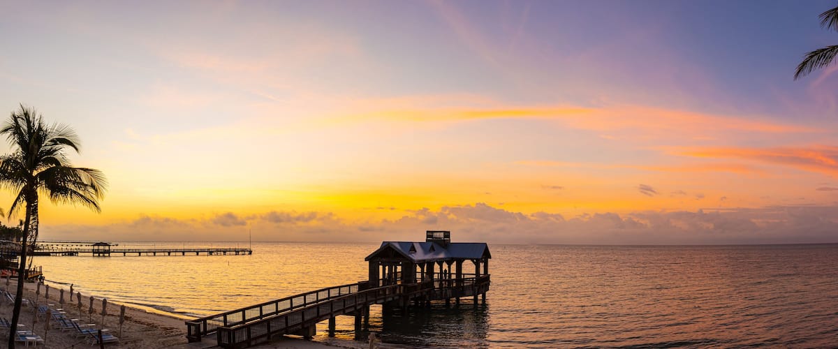 A sunset over a beach with a wooden pier and a small structure on it.