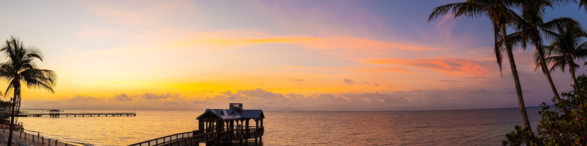 A sunset over a beach with a wooden pier and a small structure on it.