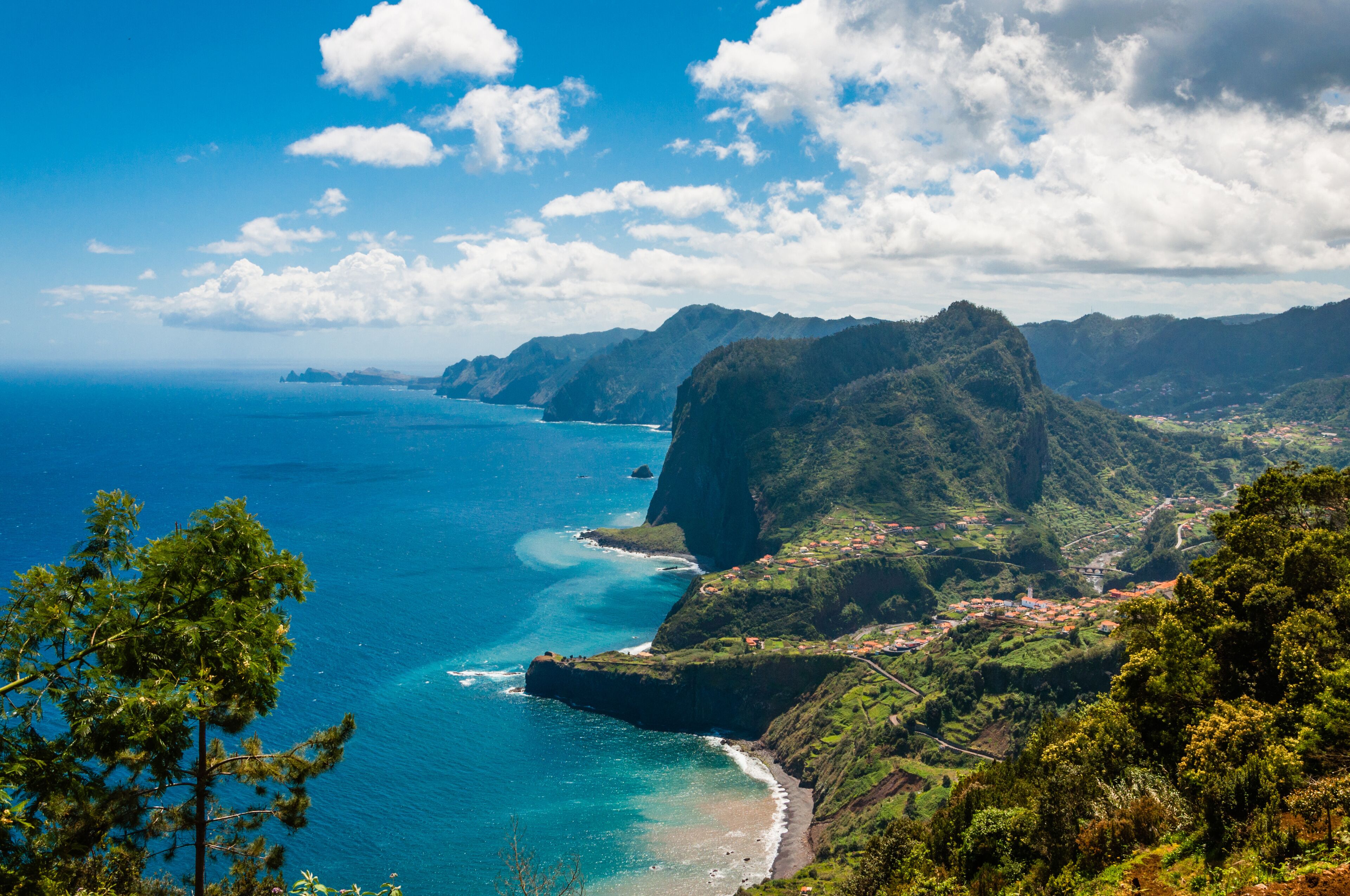A coastal landscape with a prominent mountain, a clear blue sea, and a small village.