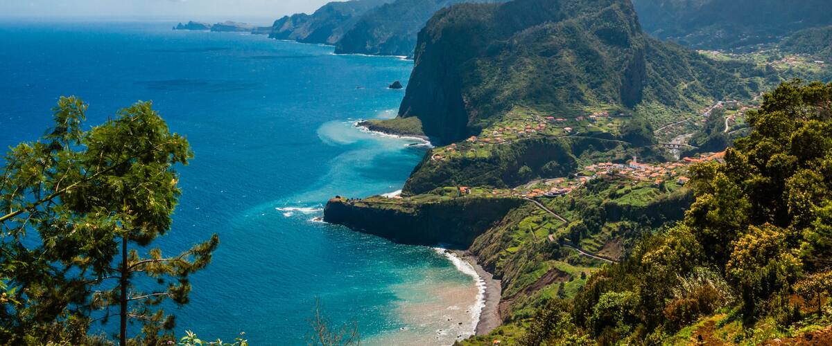 A coastal landscape with a prominent mountain, a clear blue sea, and a small village.