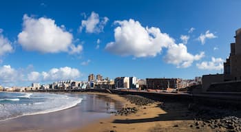Un paisaje urbano costero con playa, costa rocosa y un cielo azul despejado con nubes.