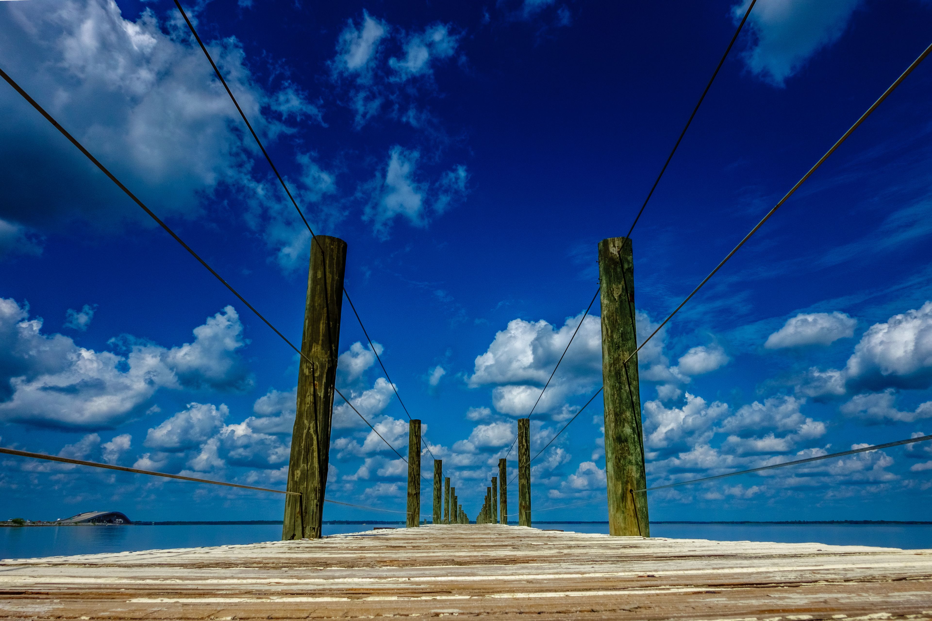 A wooden pier extending into a body of water under a blue sky with scattered clouds.