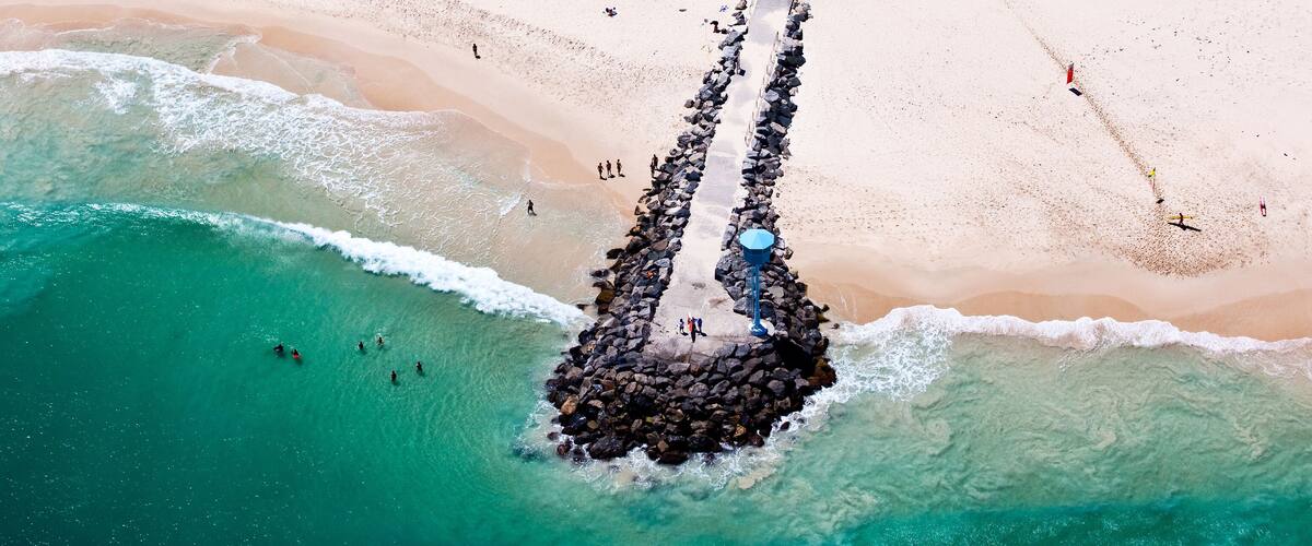 An aerial view of a beach with a rocky breakwater and clear turquoise waters.