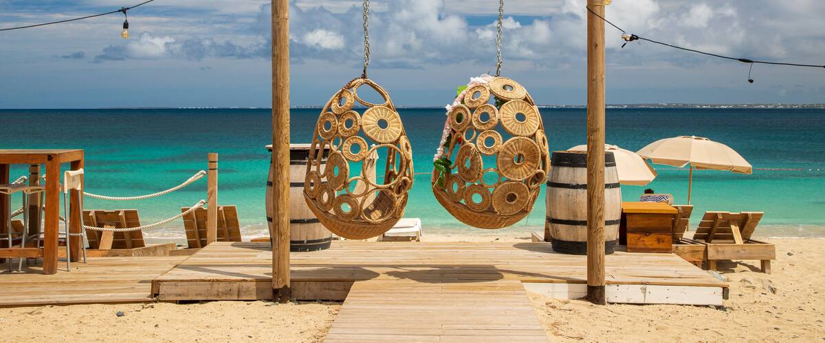 A wooden deck with hanging wicker chairs and a wooden swing set overlooking turquoise waters.