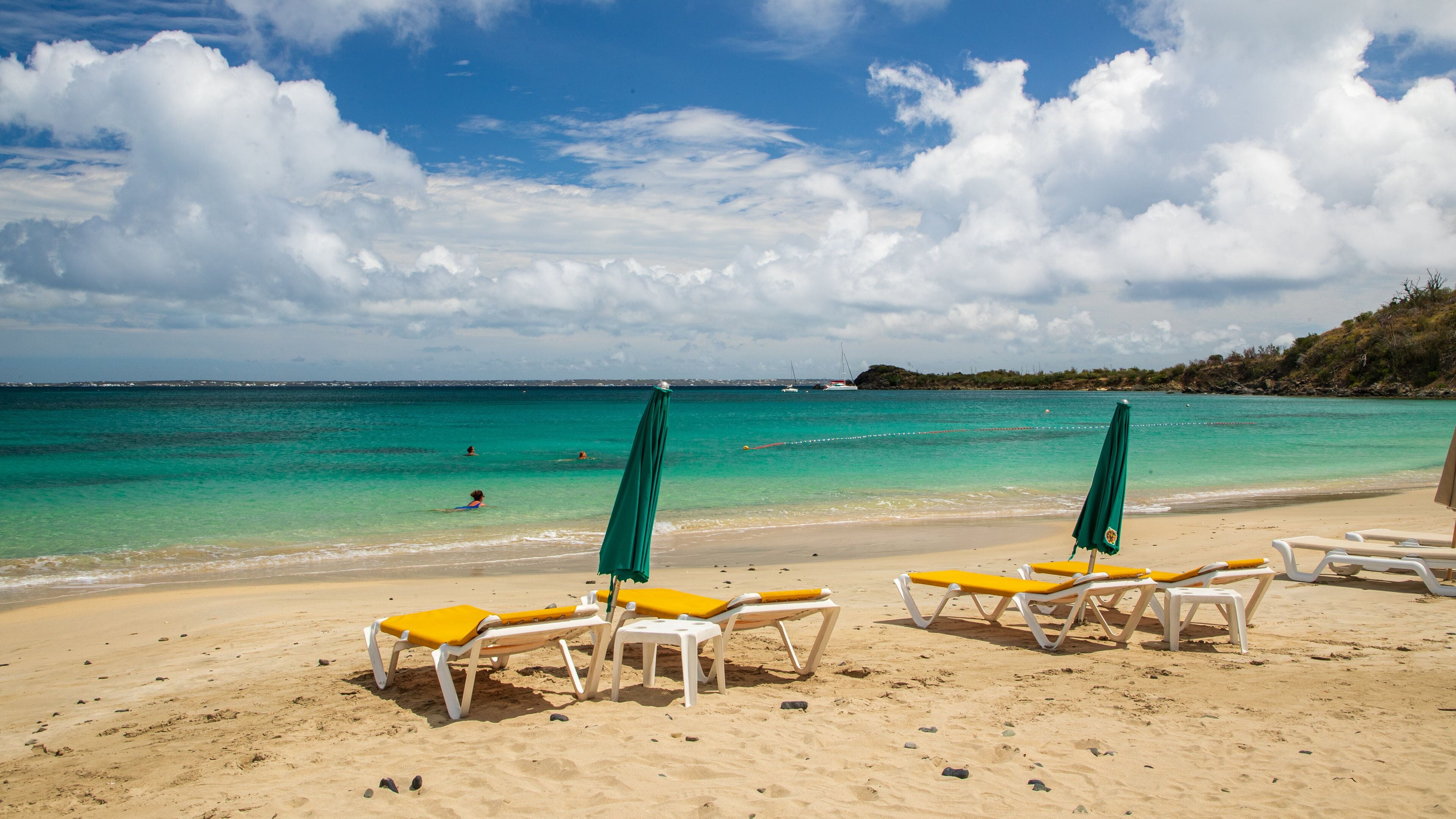 A beach with turquoise water, clear skies, and several sun loungers with green umbrellas.