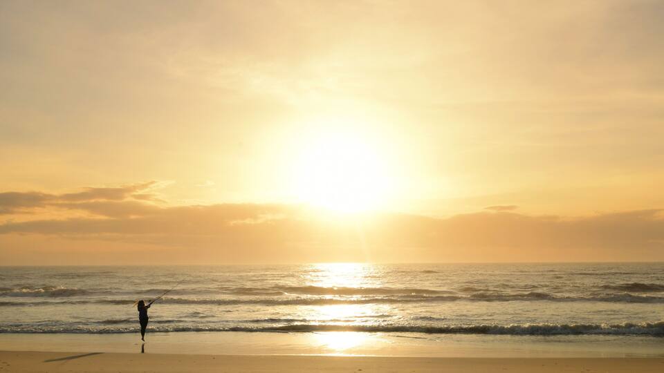 Behind teen girl casting fishing pole into ocean Outer Banks Nor