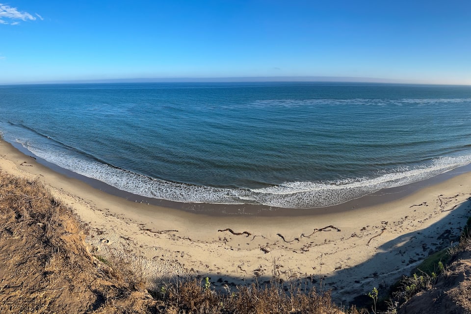 A coastal landscape with a sandy beach, ocean waves, and a clear blue sky.