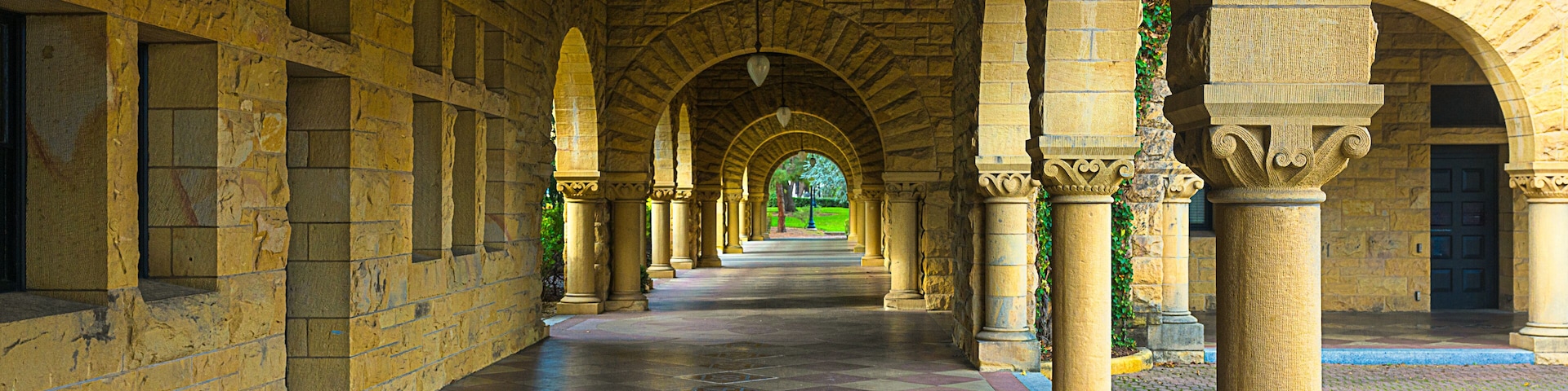 2024-01-16 BRICK BUILDING WTH ARCHES AND SQUARE WINDOWS ALONG A TILED WALKWAY WITH A GREEN PARK LIKE SCENE AT THE END OF THE WALKWAY IN PALO ALTO CALIFORNIA