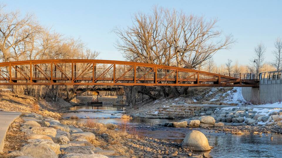 A metal bridge over a river with a cyclist on a path beside it.