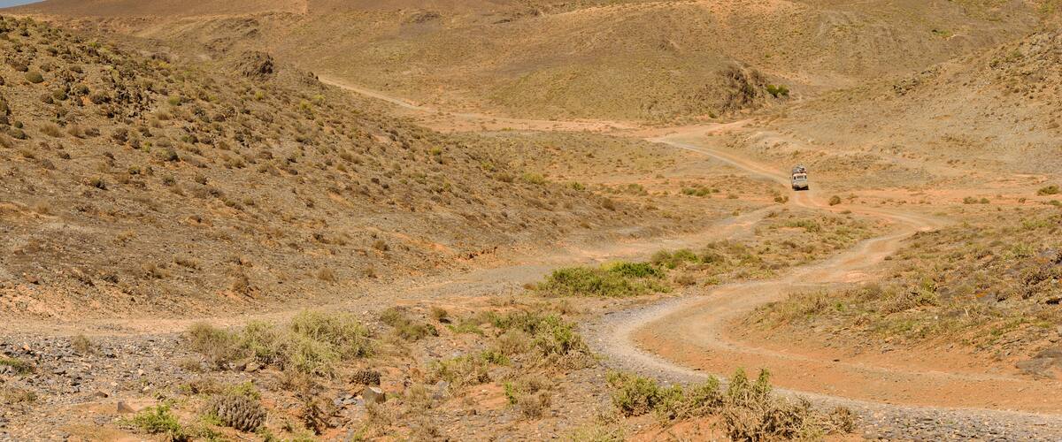 A desert landscape with a winding dirt road and a vehicle in the distance.