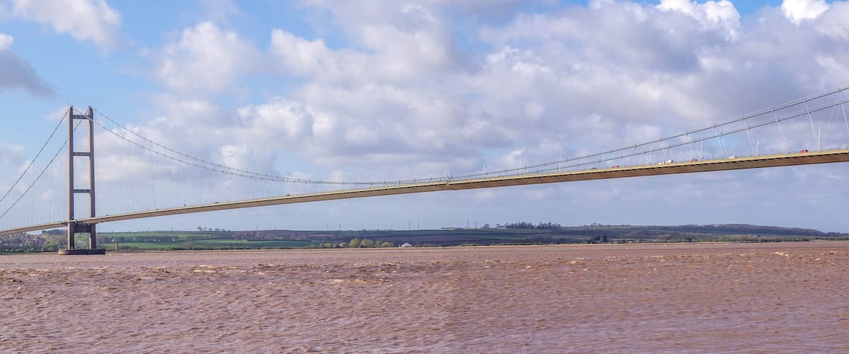 A large suspension bridge over a river with a cloudy sky.