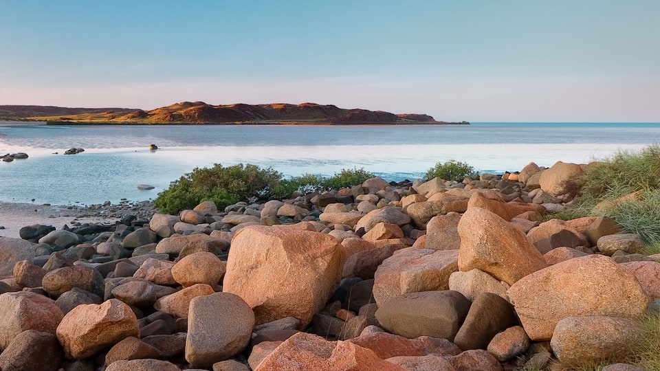 A rocky beach with large boulders and a calm sea.