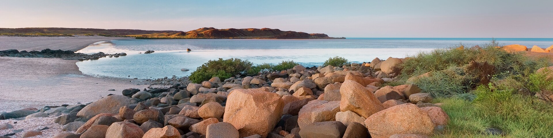 A rocky beach with large boulders and a calm sea.
