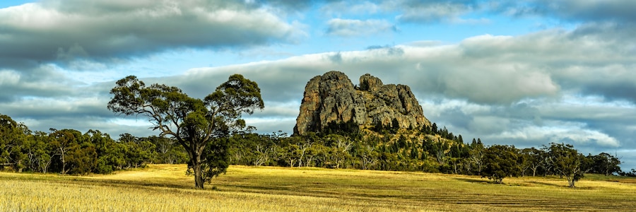 A rocky outcrop with a field in the foreground and a forested hill in the background.