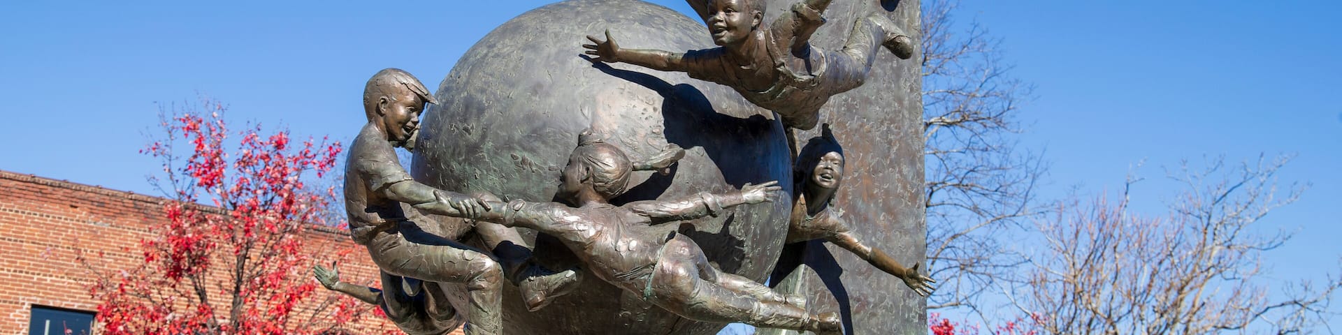 a sculpture of children flying around a globe in a gorgeous autumn landscape at the Decatur Square with red and yellow autumn trees, lush green trees and clear blue sky in Decatur Georgia USA