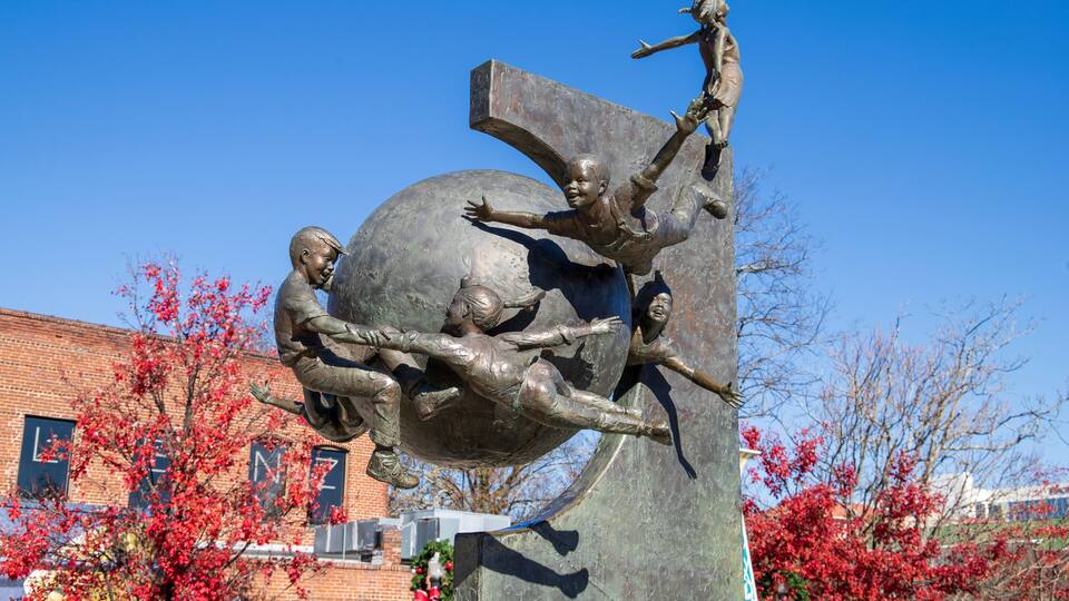 a sculpture of children flying around a globe in a gorgeous autumn landscape at the Decatur Square with red and yellow autumn trees, lush green trees and clear blue sky in Decatur Georgia USA