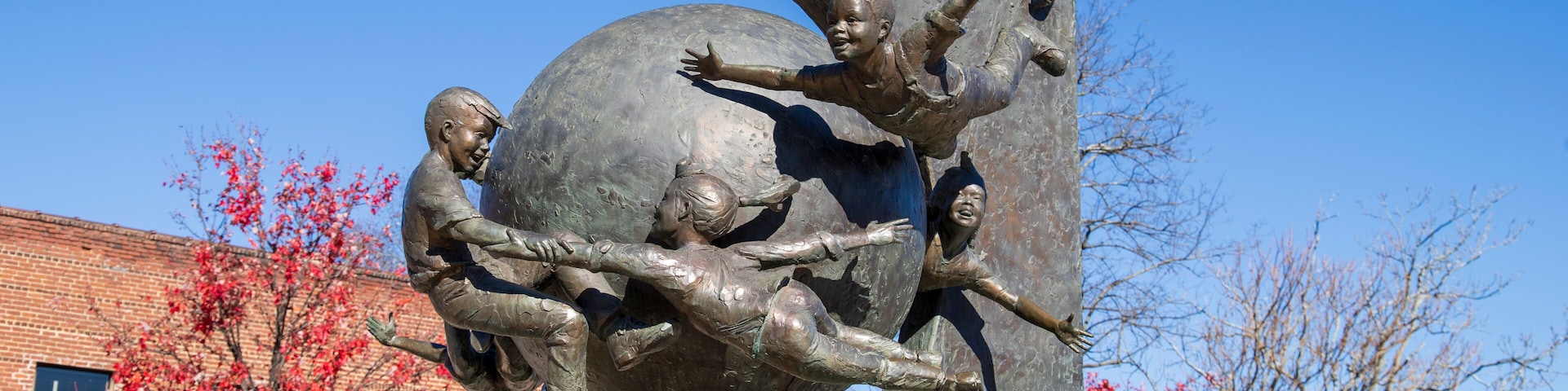 a sculpture of children flying around a globe in a gorgeous autumn landscape at the Decatur Square with red and yellow autumn trees, lush green trees and clear blue sky in Decatur Georgia USA