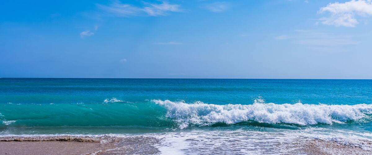 Panorama of a turquoise wave with white foam on a sandy ocean beach in Melbourne Beach, Florida