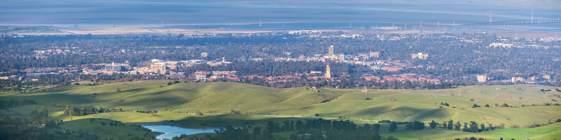 A coastal city with rolling hills, a river, and a bridge in the distance.