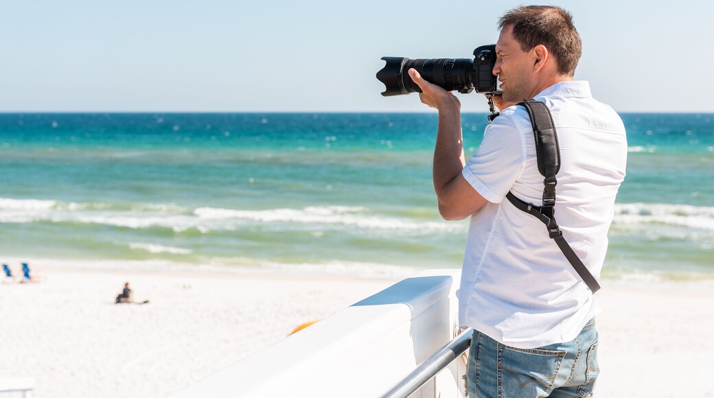 Young photographer man taking picture on beach during sunny day in Seaside, Florida panhandle town village with ocean by steps