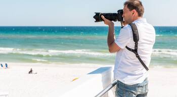 Young photographer man taking picture on beach during sunny day in Seaside, Florida panhandle town village with ocean by steps