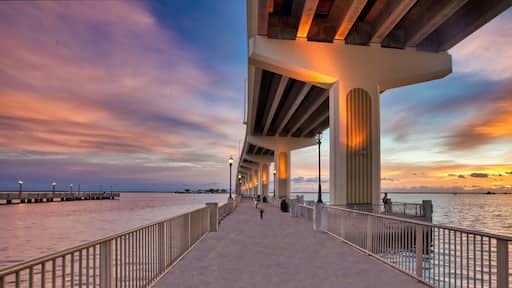 A waterfront promenade under a bridge with a sunset sky.