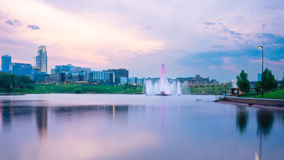 View of Omaha Nebraska skyline at sunset seen from Heartland of America Riverside Park with lake in view.