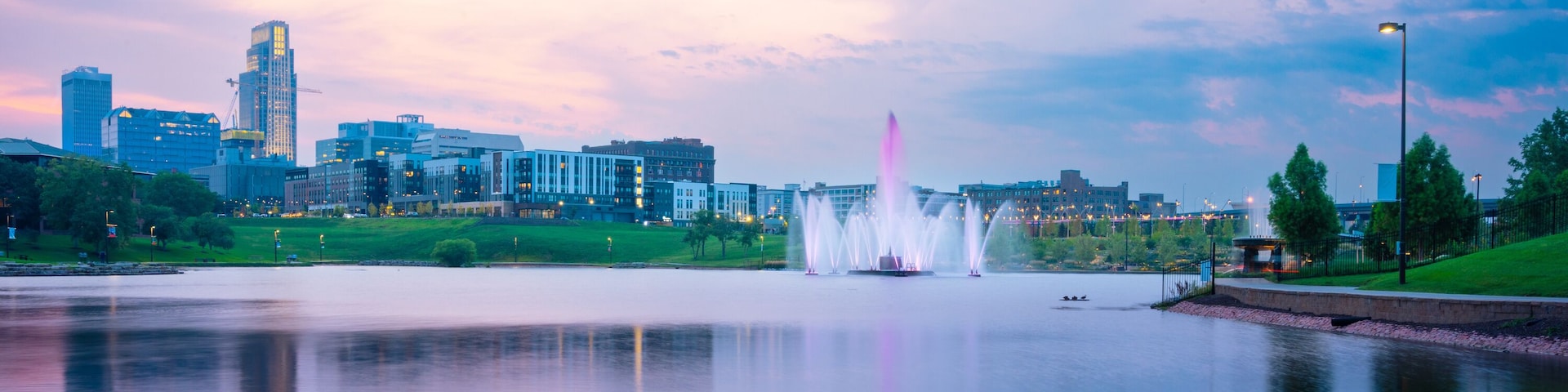 View of Omaha Nebraska skyline at sunset seen from Heartland of America Riverside Park with lake in view.