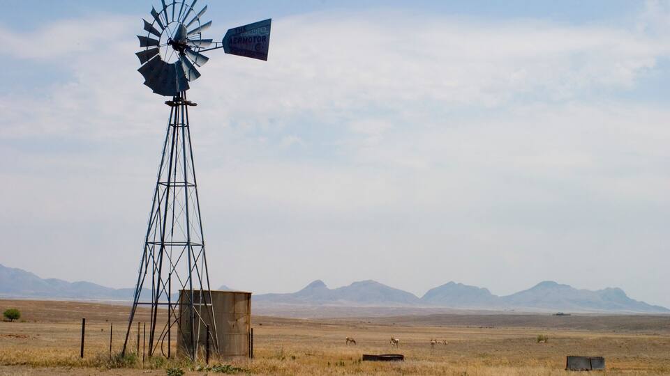 Un molino de viento en un campo abierto y extenso, con montañas al fondo.