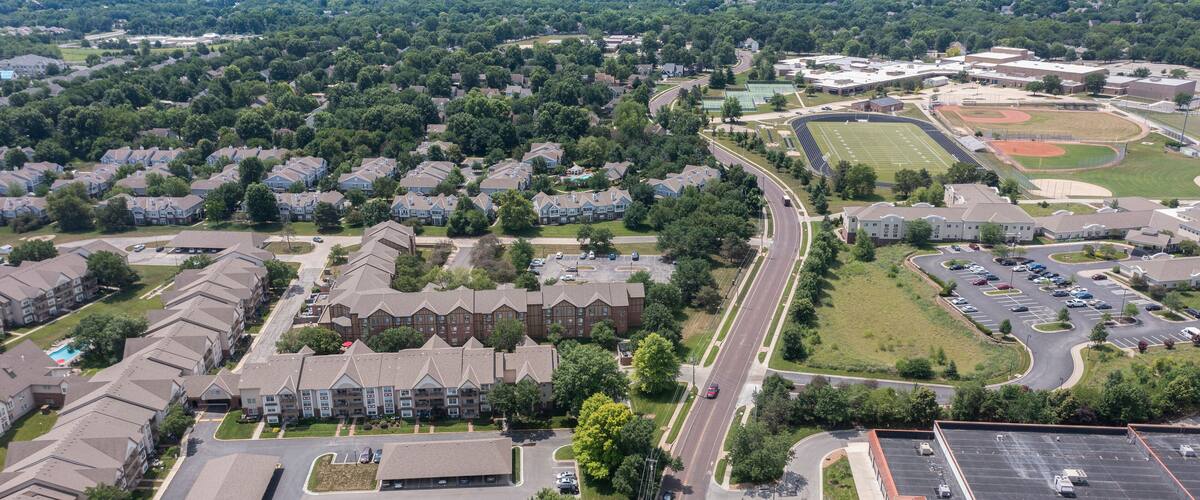 An aerial view of a suburban area with residential buildings, a sports field, and a parking lot.