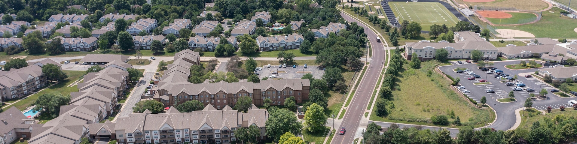 An aerial view of a suburban area with residential buildings, a sports field, and a parking lot.