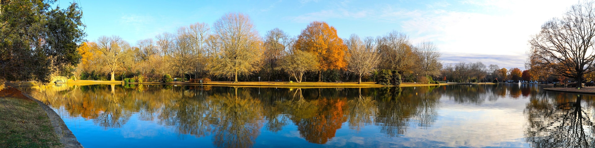 a panoramic shot of a gorgeous autumn landscape with lake and autumn colored trees reflecting off the water with blue sky and clouds at Freedom Park in Charlotte North Carolina USA