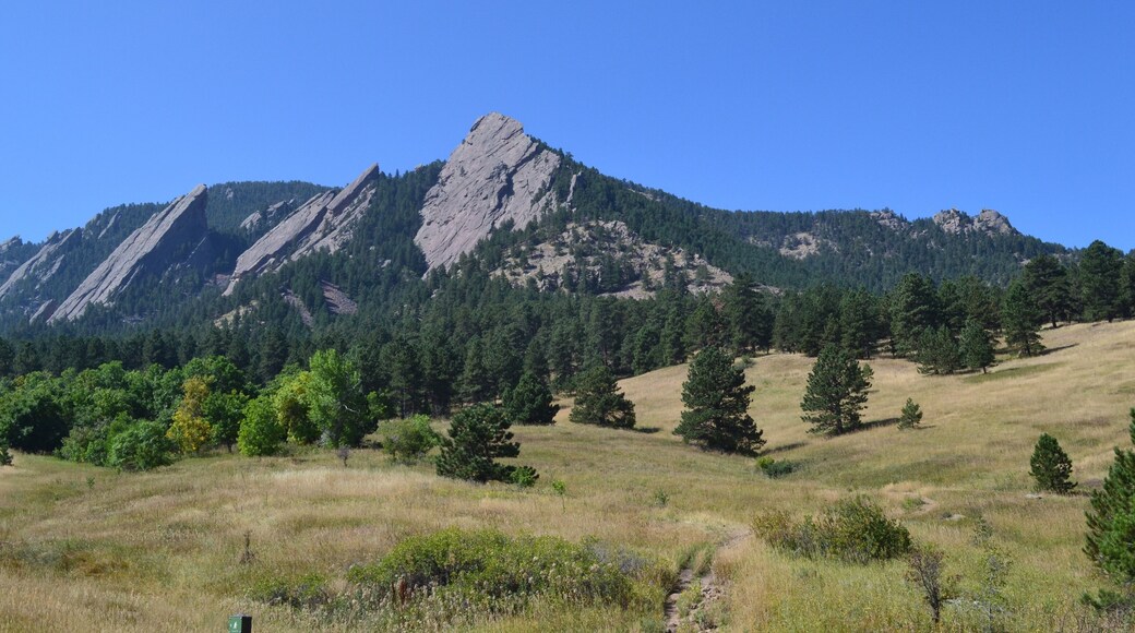 Mountain peak and ridge of the Flat Irons, with bright blue sky, pine trees and hiking trails in Boulder, Colorado.