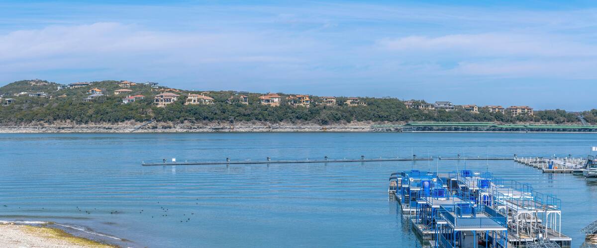 Panoramic view of Lake Austin with docked party boats near residences at Austin, Texas. There are flat boats on the right below near the shore across the sloped residential area across.