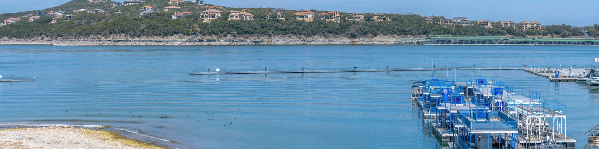 Panoramic view of Lake Austin with docked party boats near residences at Austin, Texas. There are flat boats on the right below near the shore across the sloped residential area across.