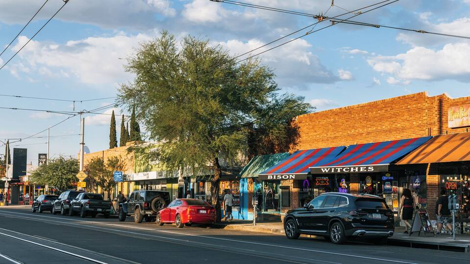 A street with cars, a red car parked on the side, and a building with a sign that reads 'WITCHES'.