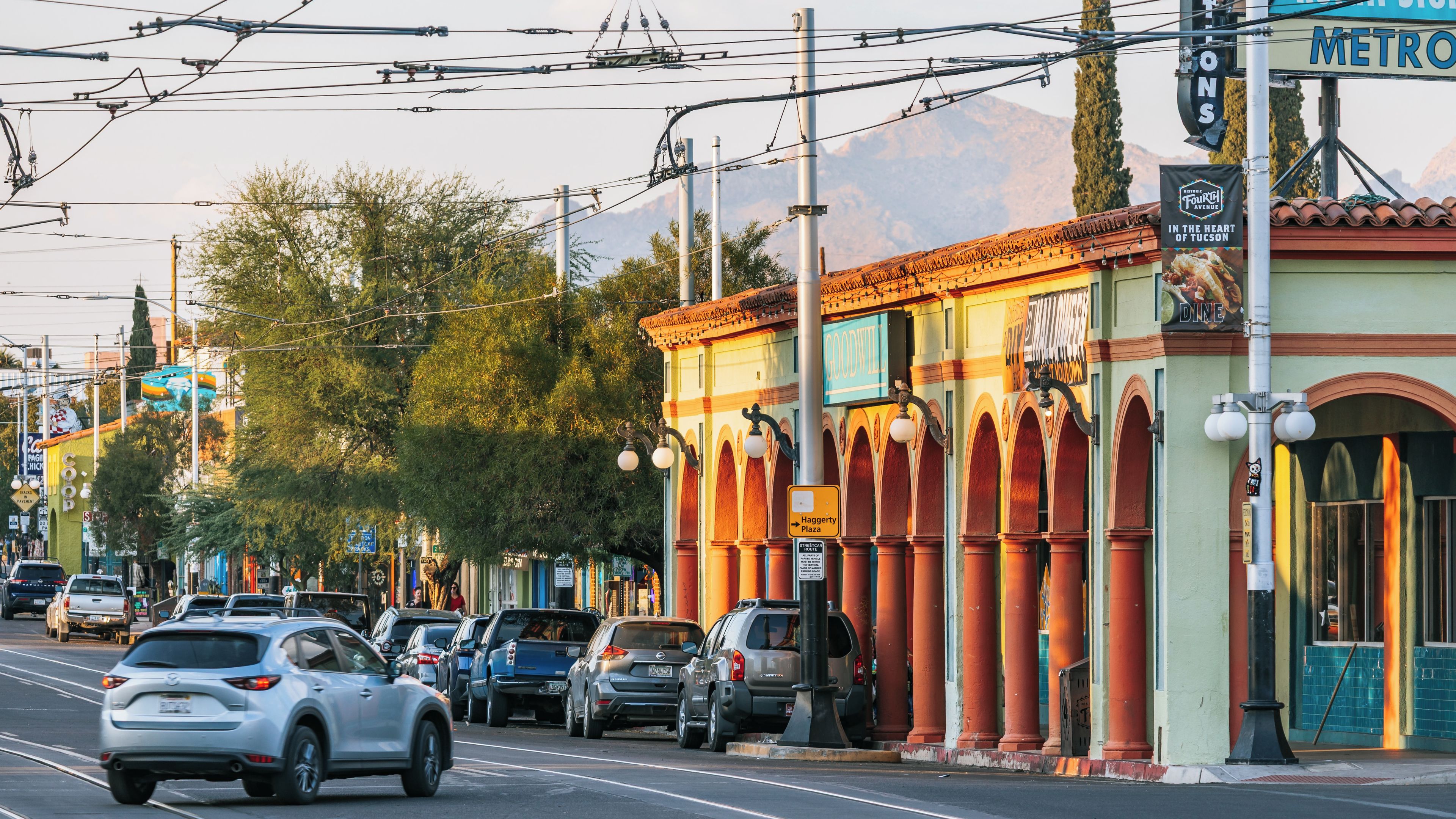 A street lined with parked cars, a building with a sign for 'Goodnight Plaza,' and overhead power lines.