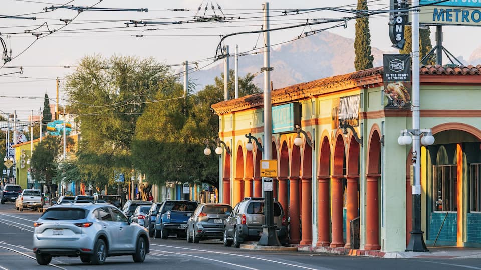 A street lined with parked cars, a building with a sign for 'Goodnight Plaza,' and overhead power lines.