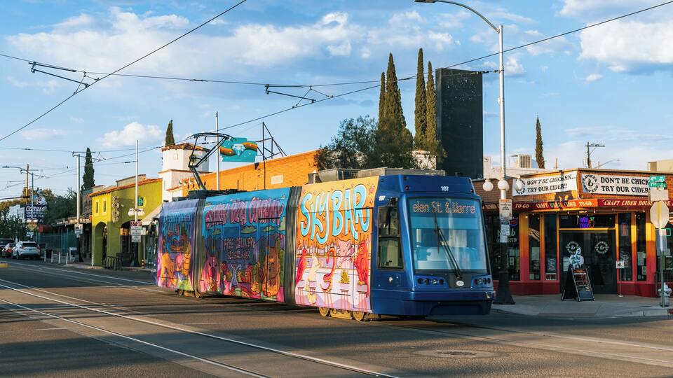 A colorful trolley with a vibrant mural, a street with shops, and a clear sky.