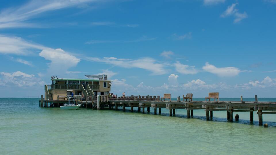 Old wooden fishing pier with building, people, tropical beach, blue sky.