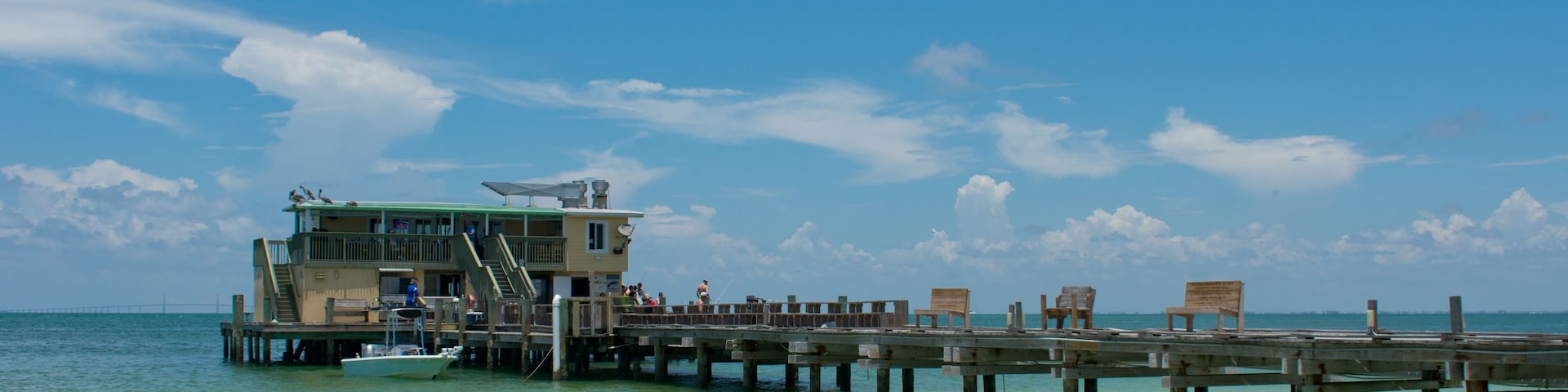 Old wooden fishing pier with building, people, tropical beach, blue sky.