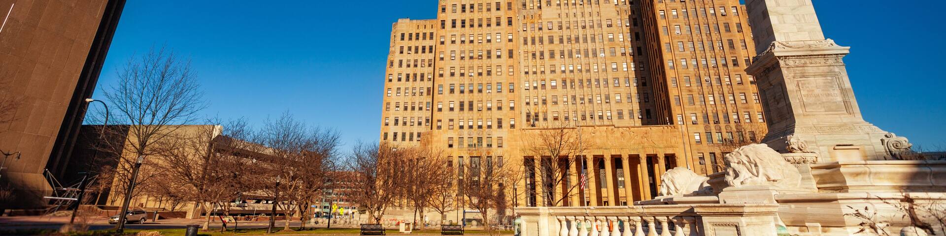 A tall building with a distinctive Art Deco style, a large obelisk monument, and a clear blue sky.