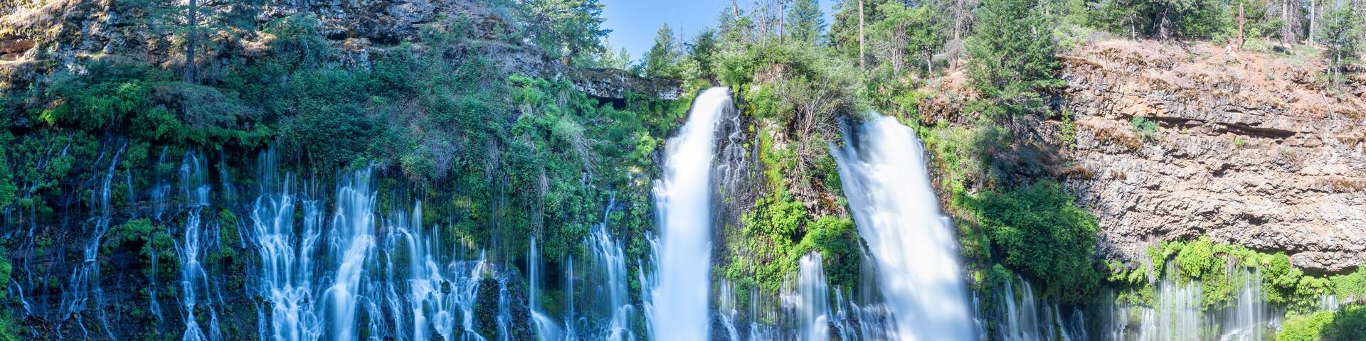 A multi-tiered waterfall surrounded by dense forest.