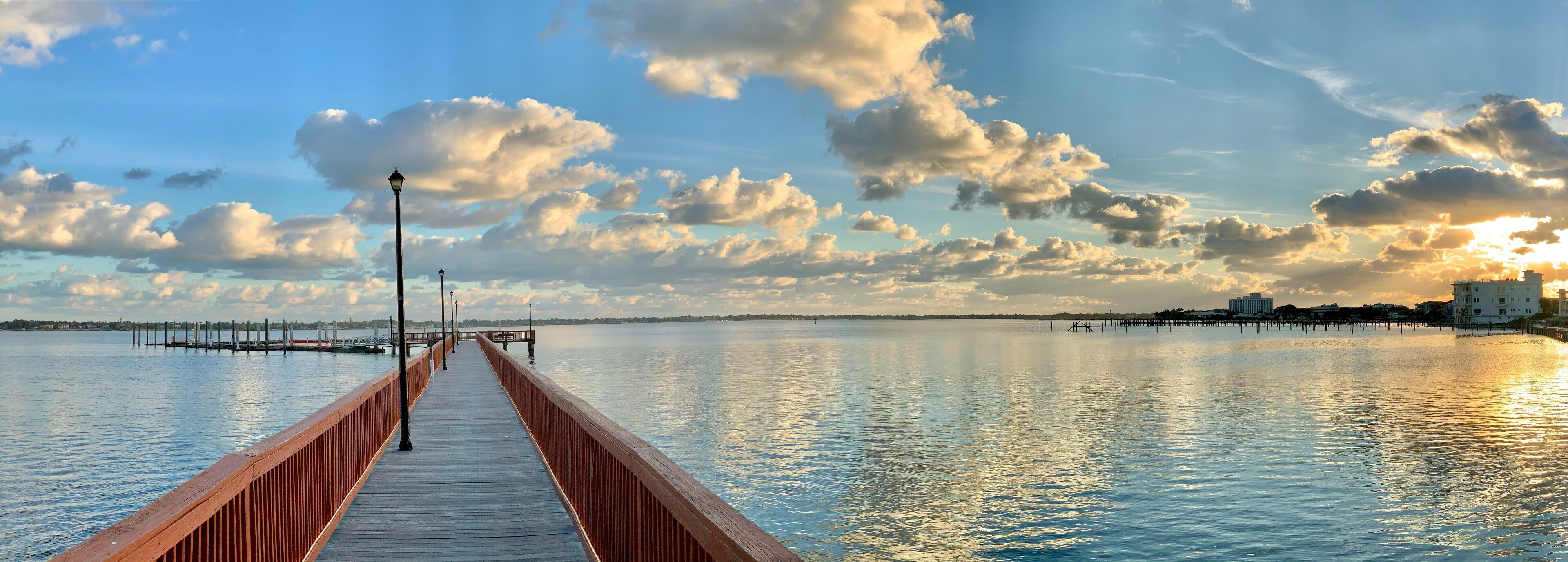 A wooden pier extending into calm water with a sunset in the background.