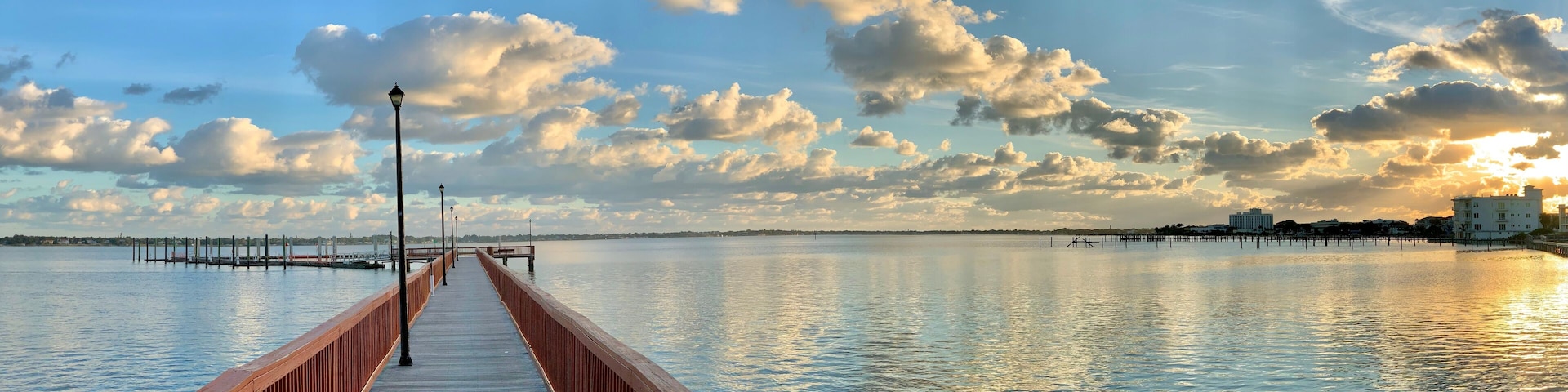 A wooden pier extending into calm water with a sunset in the background.
