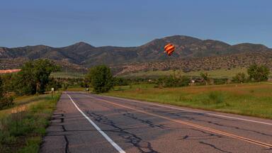 A road with mountains in the background and a hot air balloon flying.
