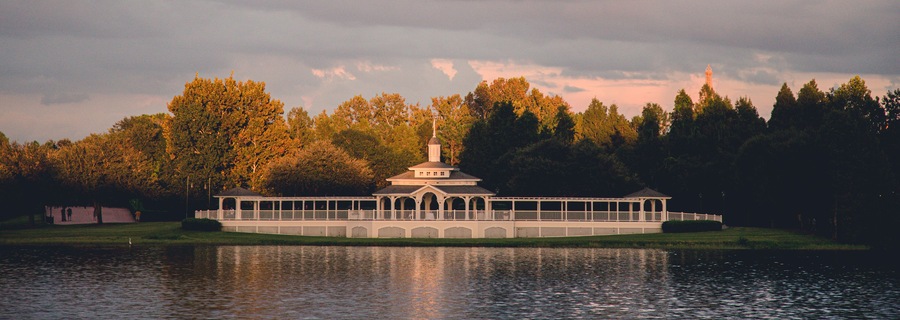 Un barco de vapor blanco atracado en un lago, con un pabellón y una torre, rodeado de árboles y un cielo nublado.